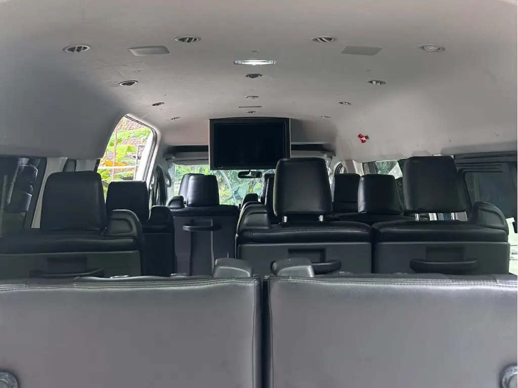 Interior of a Nusa Indah Transport HiAce with dark seats and a TV